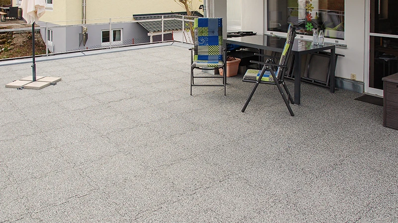 A rooftop area features grey marbled WARCO terrace tiles made from PU-bonded rubber granulate. Their puzzle interlocking ensures a precise fit, combining weather resistance with durability. The stable material reduces footstep noise and contributes to a tidy, well-maintained look. It also provides slip resistance and comfortable footing, making the flooring particularly user-friendly.