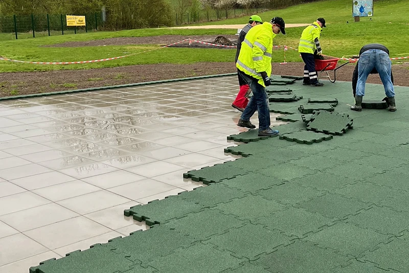 A group of workers laying green WARCO Outdoor click tiles in the rain on a tiled outdoor area.