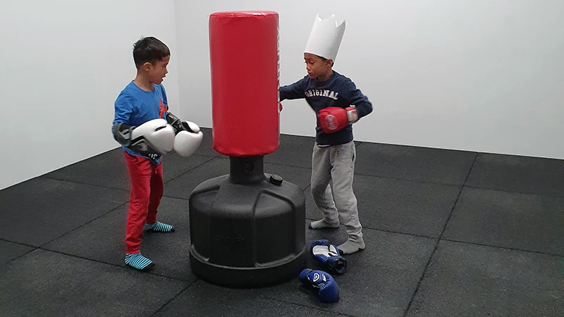 2 children boxing on punching bag, black fitness mat from WARCO offers good fall protection and support.