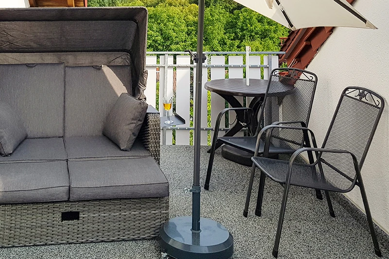 This photo shows a balcony covered with grey WARCO floor tiles. A comfortable beach chair and a small table with two metal chairs provide a spot to relax and enjoy. The elastic, slip-resistant flooring protects against moisture and helps reduce footstep noise. It is also low-maintenance and weatherproof, keeping the outdoor area looking great and inviting for a long time.