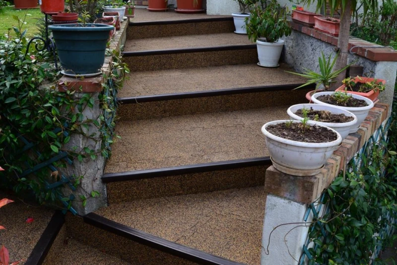 Brown steps in the garden lead past flower pots towards the terrace in the garden. Warco stair covering makes them sure-footed.