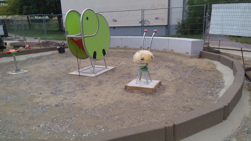 A small children's playground in the form of a round island is currently under construction. The play equipment has already been installed and the base layer for the ground has been laid. The area is edged with chain elements, i.e. interconnected block steps made of rubber granulate.