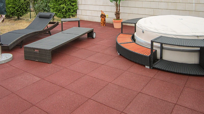 A spacious outdoor area with red WARCO terrace tiles made of PU-bonded rubber granulate that provide comfortable footing and lasting durability. Furnished with cozy garden furniture and a whirlpool blending seamlessly into the design. The elastic surface absorbs footfall, resists weather, and requires minimal maintenance. Its slip-resistant texture offers an appealing solution for stylish outdoor relaxation. Ideal for modern terraces seeking both functionality and comfort.